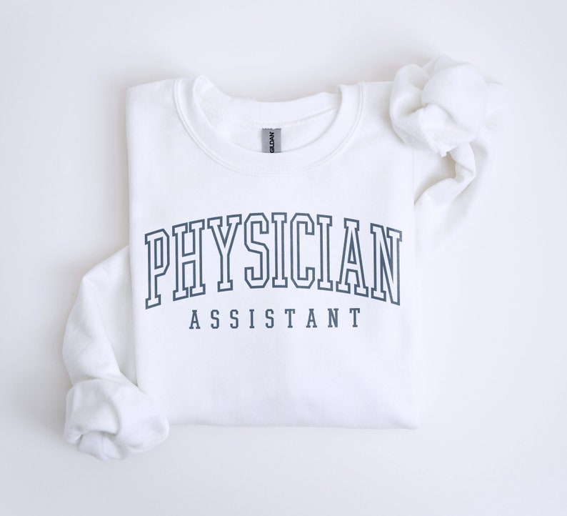 K&ouml;nnte beinhalten: Wei&szlig;er Pullover mit dem Text "PHYSICIAN ASSISTANT" in einer dunkelblauen College-Schrift.