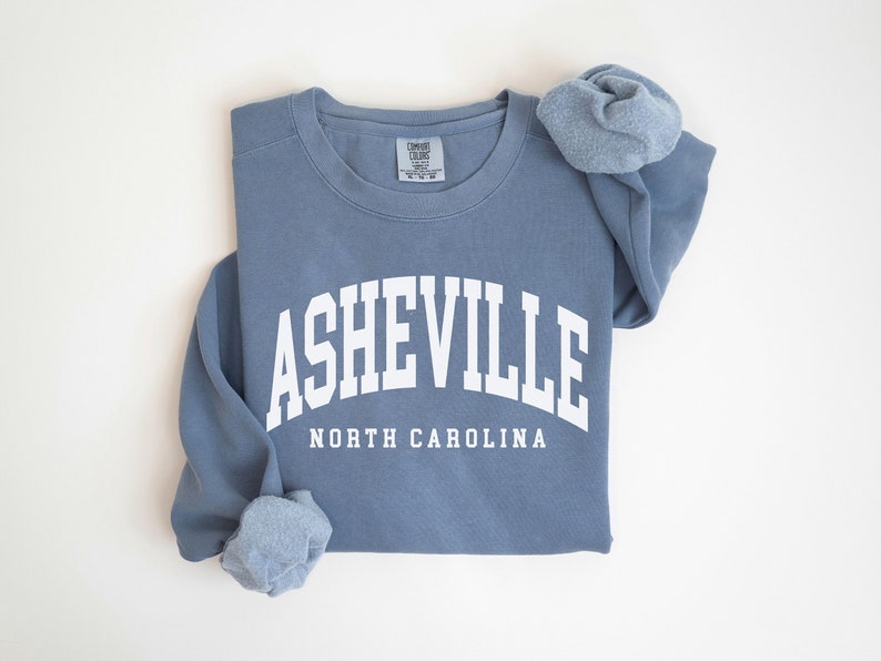 May include: A blue sweatshirt with the text 'ASHEVILLE NORTH CAROLINA' in white lettering.