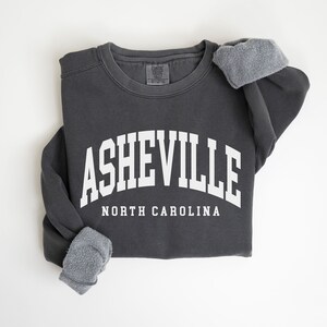 May include: A charcoal gray sweatshirt with a white arch design that reads "Asheville North Carolina".