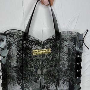May include: A black lace handbag featuring a 3MF digital file design, black handles, and side lacing details. A gold rectangular plaque is centered on the front. The text 3MF DIGITAL FILE 3D Printable Lace Handbag is visible at the top.