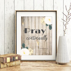 May include: A framed print with a woodgrain background and white flowers. The print features the text "Pray continually" with a scripture reference from 1 Thessalonians 5:17.