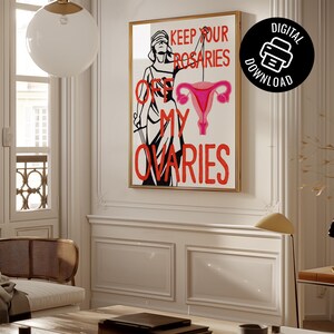 A vertical mockup of the "Keep Your Rosaries Off My Ovaries" feminist poster in a gold frame, hanging in a bright, modern Parisian-style living room with white paneled walls.