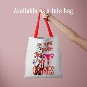 A white canvas tote bag with red handles being held against a pink background. The bag features the "Keep Your Rosaries Off My Ovaries" design. Text at the top reads: "Available as a tote bag."