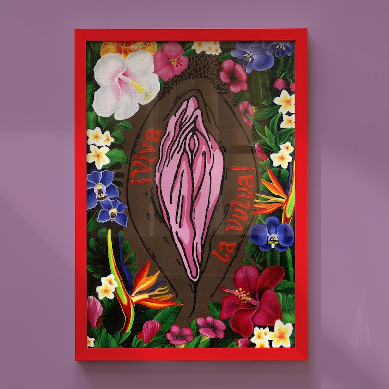The "¡Viva la vulva!" art print with a deep brown skin tone background and orange-red typography, displayed in a bright red frame against a lavender wall.