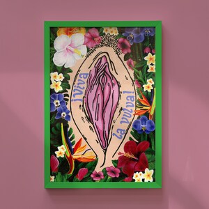 Vibrant Viva La Vulva art print featuring a pink vulva illustration surrounded by tropical flowers like hibiscus and birds of paradise, displayed in a bright green frame against a mauve wall.