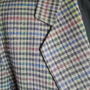 Puede incluir: Primer plano de una chaqueta gris con un estampado de cuadros multicolor. La tela tiene una textura sutil y la chaqueta tiene un estilo clásico.