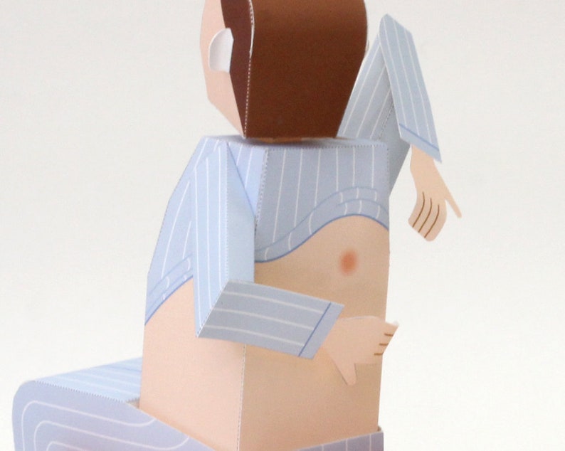 May include: A paper craft figure of a person with brown hair wearing a light blue and white pinstriped shirt that is lifted to reveal the torso. The figure has light skin, articulated arms, and is seated on a matching pinstriped surface.