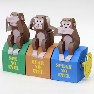May include: Three papercraft monkeys sitting on coloured boxes. The green box says SEE NO EVEL, the orange box says HEAR NO EVEL, and the blue box says SPEAK NO EVEL. The first monkey covers its eyes, the second its ears, and the third its mouth.