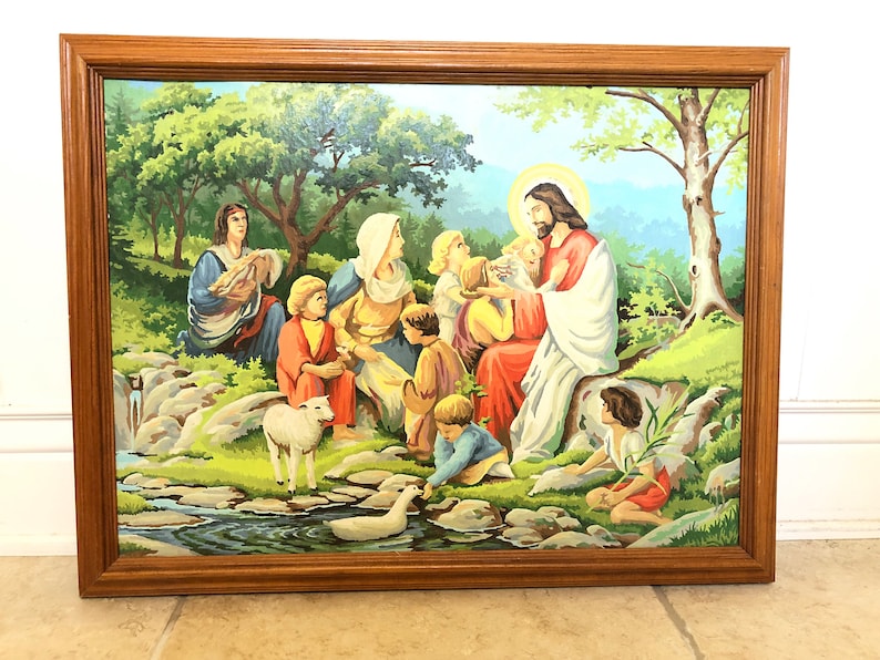 Peut inclure: Une peinture encadr&eacute;e repr&eacute;sentant J&eacute;sus entour&eacute; d'enfants dans un paysage verdoyant luxuriant. La peinture repr&eacute;sente un ruisseau, un agneau et un canard. Les couleurs sont vives et vibrantes, avec des nuances de vert, bleu, rouge et jaune.