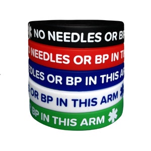 Puede incluir: Cinco pulseras de silicona en negro, rojo, azul, blanco y verde con el texto "NO NEEDLES OR BP IN THIS ARM" y un símbolo de estrella médica.