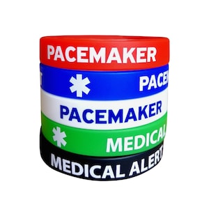 Puede incluir: Conjunto de cuatro pulseras de alerta médica de silicona. La pulsera superior es roja con texto blanco que dice "PACEMAKER". La segunda pulsera es azul con un símbolo blanco de estrella de la vida y texto blanco que dice "PACEMAKER". La tercera pulsera es blanca con texto negro que dice "PACEMAKER". La pulsera inferior es verde con un símbolo blanco de estrella de la vida y texto blanco que dice "MEDICAL ALERT".