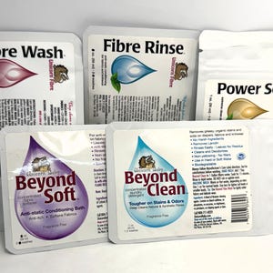 May include: An assortment of laundry care products, including Fibre Wash, Fibre Rinse, Power Scour, Beyond Soft, and Beyond Clean. Each product is packaged in a white packet with a colorful droplet design and the "Unicorn Fibre" logo. The products are designed for fabric care.