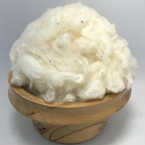 May include: A white, fluffy pile of cotton fiber in a wooden bowl.
