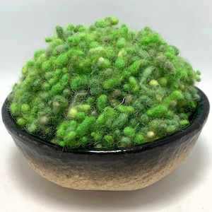 May include: A ceramic bowl with a dark brown rim and a light brown base is filled with vibrant green, textured wool roving. The wool has varying shades of green and yellow, creating a natural, organic appearance. The bowl is set against a white background.
