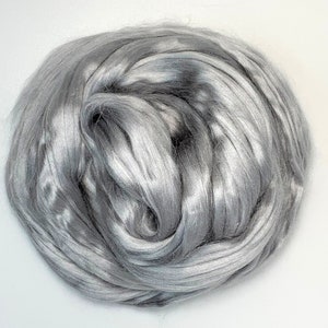 Może przedstawiać: Zbliżenie na stos srebrnych włókien. Włókna są miękkie i puszyste, a mają delikatny połysk.