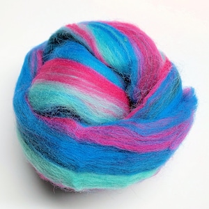 May include: A vibrant ball of wool roving in shades of blue, turquoise, and magenta. The wool fibers are tightly packed, creating a soft, textured appearance. Ideal for fiber art projects, this roving offers a blend of colors.