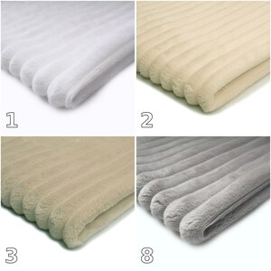 May include: A collection of four folded blankets featuring a soft, plush texture with a distinct ribbed or channel-tufted pattern. The blankets are presented in four different solid colors: bright white, cream, light tan, and cool light gray.