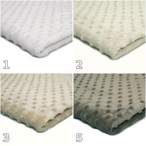 Può includere: Una collezione di quattro coperte piegate caratterizzate da una texture a pois in rilievo. Le coperte sono presentate in quattro distinti colori neutri: bianco brillante, crema, beige chiaro e grigio medio. Ogni coperta è contrassegnata da un numero.