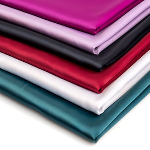 Peut inclure: Une pile de six tissus de satin de couleurs différentes. Les tissus sont disposés dans un dégradé de couleurs, allant du violet foncé au vert sarcelle.