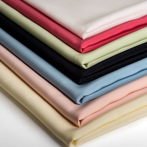 Peut inclure: Un assortiment d'échantillons de tissu de différentes couleurs, dont le blanc, le rose, le bleu clair, le bleu foncé, le vert et le rouge. Le tissu est lisse et semble être en coton.