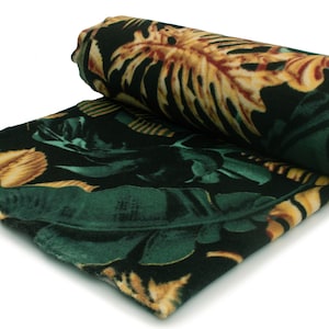May include: A rolled up green and gold tropical print fleece blanket. The blanket has a dark green background with large yellow and orange leaves.