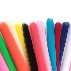 May include: A collection of tulle fabric rolls arranged in a fan shape, featuring a vibrant spectrum of colors including bright pink, green, orange, cream, yellow, black, red, light pink, turquoise, dark blue, white, and magenta.