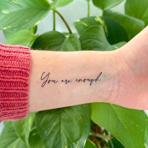 Op de afbeelding: Een close-up van iemands pols met een tatoeage die "You are enough" zegt.