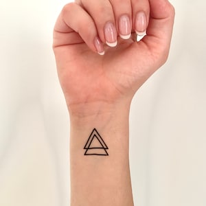 Puede incluir: Un dibujo simple de dos triángulos superpuestos en negro en la muñeca de una persona.