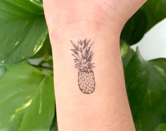 May include: A black and white line drawing of a pineapple on a person's wrist.