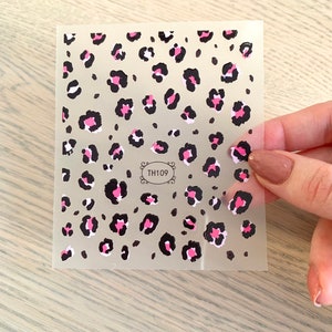 Op de afbeelding: Een vel nagelstickers met een luipaardprint. De stickers zijn zwart, roze en wit op een transparante achtergrond. Het vel heeft de code "TH109" erop gedrukt.