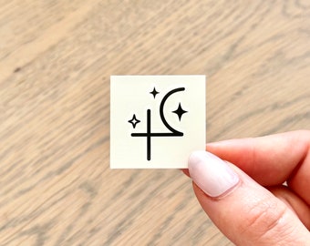 May include: A white square sticker with a black crescent moon, a cross, and three stars. The sticker is a celestial design.