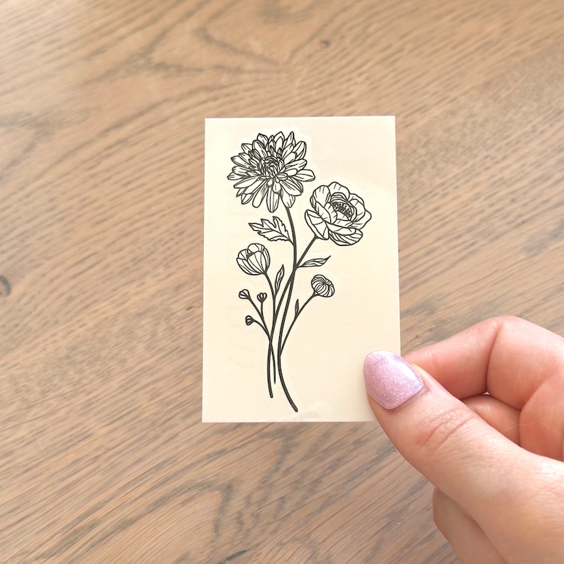 May include: A black and white line drawing of a bouquet of flowers. The bouquet includes a large flower with multiple petals, a smaller flower with five petals, and several buds.