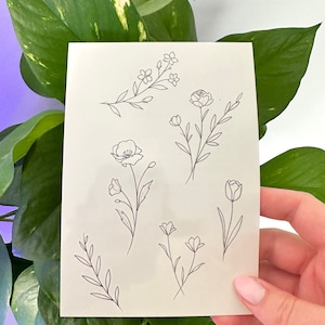 Op de afbeelding: Een vel papier met zeven eenvoudige lijntekeningen van bloemen en bladeren. De tekeningen zijn in zwarte inkt op een witte achtergrond.
