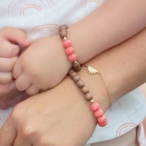 May include: Two matching bracelets with wooden beads and pink accents. The bracelet on the left has a sun charm.