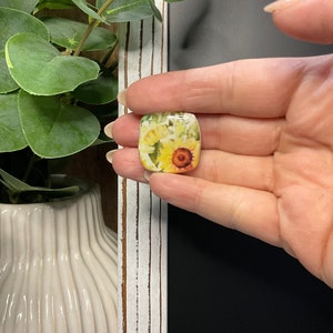 May include: A square ceramic tile with a floral design featuring yellow and white sunflowers. The tile has a glossy finish.