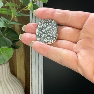 May include: A white oval ceramic tile with a black and white lace pattern.