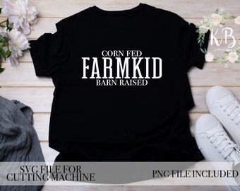 May include: Black t-shirt with white text that reads "Corn Fed Farmkid Barn Raised". The shirt is laying flat on a wooden surface with a gray sweater and white sneakers nearby.