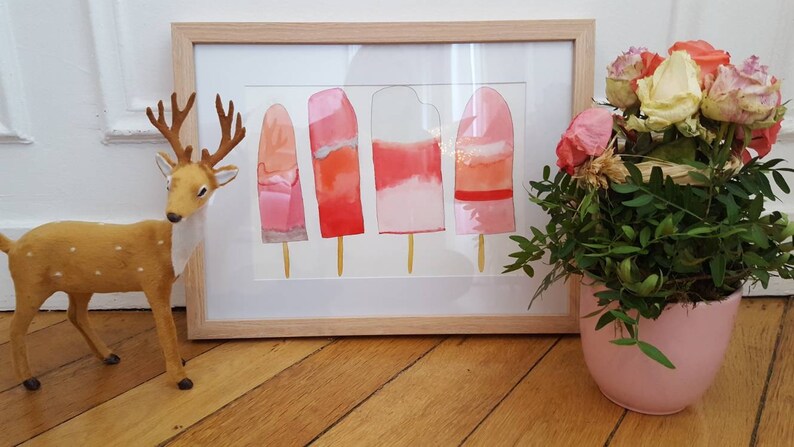 May include: A framed watercolor painting of four pink and orange popsicles on a white background. The painting is in a light wood frame and is sitting on a wooden floor.