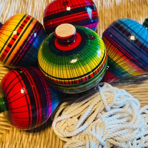 May include: A group of brightly coloured wooden spinning tops and a white rope. The tops are painted with rainbow stripes in red, yellow, green, and blue. A traditional toy.