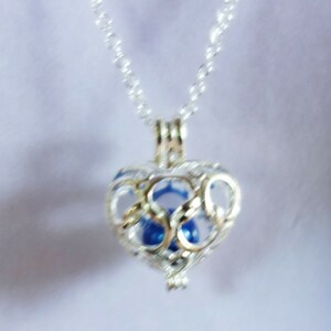 May include: A silver heart-shaped cage necklace with a blue orb inside. The cage is intricately designed with a delicate pattern.