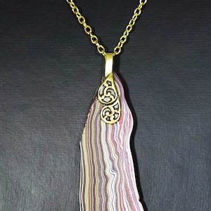 Può includere: Una collana con catena dorata con un ciondolo in agata colorata con un designo in filigrana dorata.