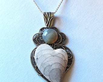 Puede incluir: Un collar de cadena de plata con un colgante en forma de corazón. El colgante presenta un corazón de piedra gris y blanco con una piedra redonda gris más pequeña engastada en un diseño de filigrana.