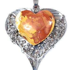 Peut inclure: Un pendentif en argent en forme de cœur avec un motif floral détaillé et une grande pierre multicolore en forme de cœur au centre.