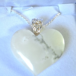 May include: A white heart-shaped pendant necklace with a silver chain and a silver filigree bail. The pendant has a marbled pattern.