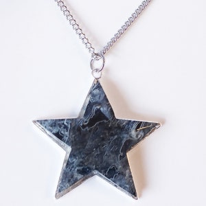 Puede incluir: Un collar de cadena de plata con un gran colgante de estrella de mármol negro y blanco.