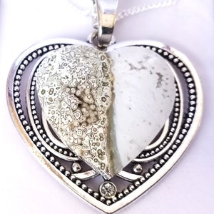 May include: A silver heart-shaped pendant featuring a white and green agate stone. The pendant has an ornate border and a small rhinestone at its centre.