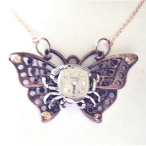 May include: A bronze butterfly necklace with a vintage watch face in the center. The watch face has black hands and Roman numeral markings. The butterfly wings are detailed with cutouts and have a gold-toned finish.