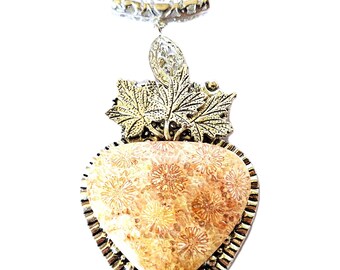 Puede incluir: Un collar con colgante en forma de corazón con un centro de piedra marrón claro, enmarcado en metal plateado y dorado. El colgante presenta un patrón floral y está adornado con detalles de hojas. El collar tiene una delicada cadena plateada.