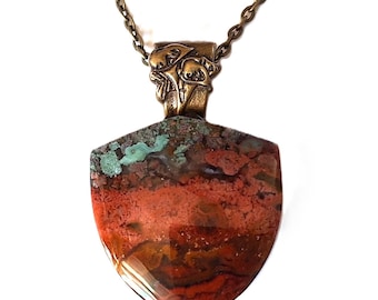 May include: Shield-shaped pendant necklace with a bronze-coloured chain. The pendant features a shield-shaped stone with red, brown, and green hues. The pendant is attached to a bronze-coloured decorative bail.