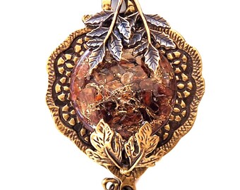 May include: Ornate pendant necklace with a bronze-colored frame and a central orb filled with amber-colored stones. The pendant features leaf and grape cluster details, suspended from a delicate chain.